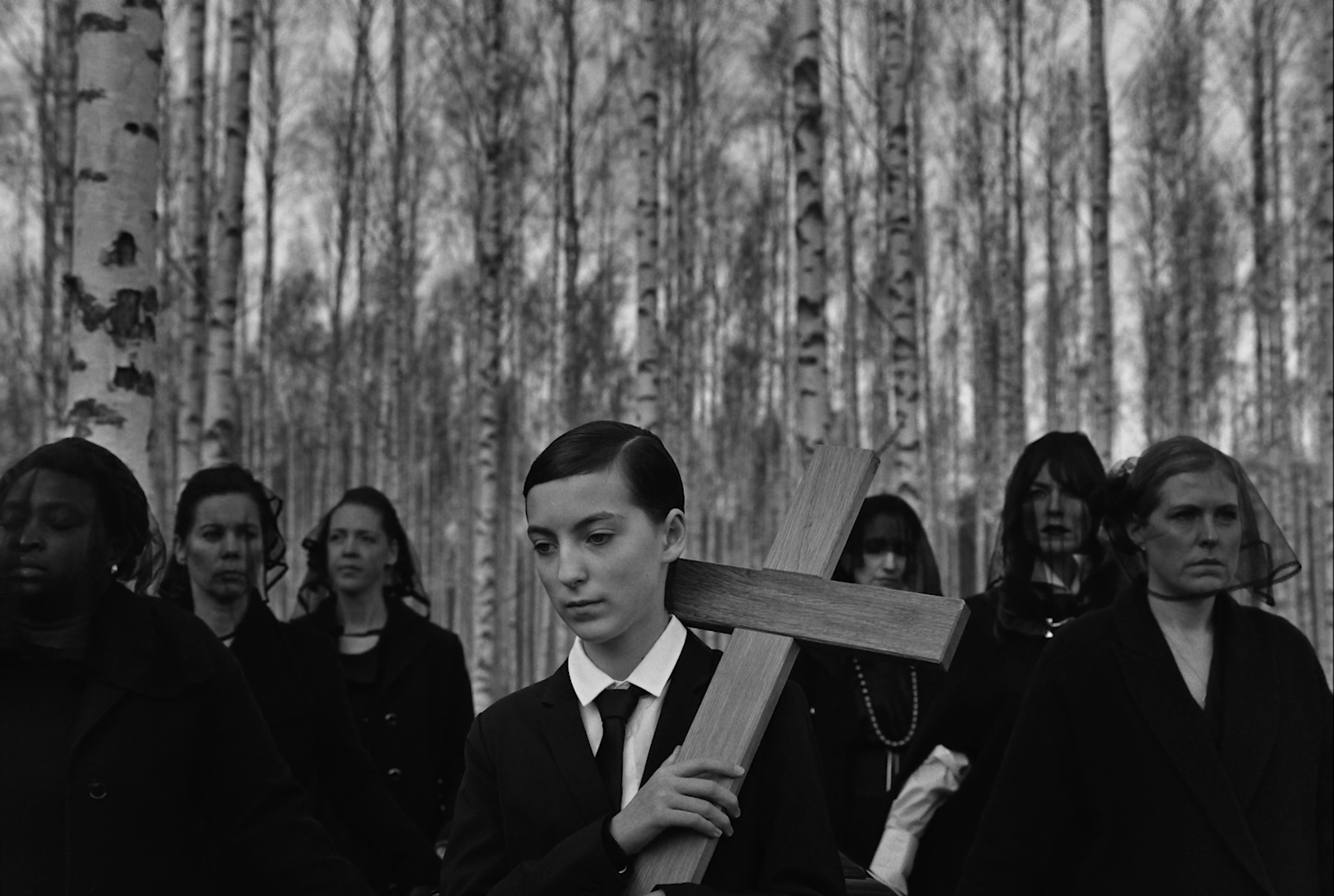 A young person holding a cross in a birch forest